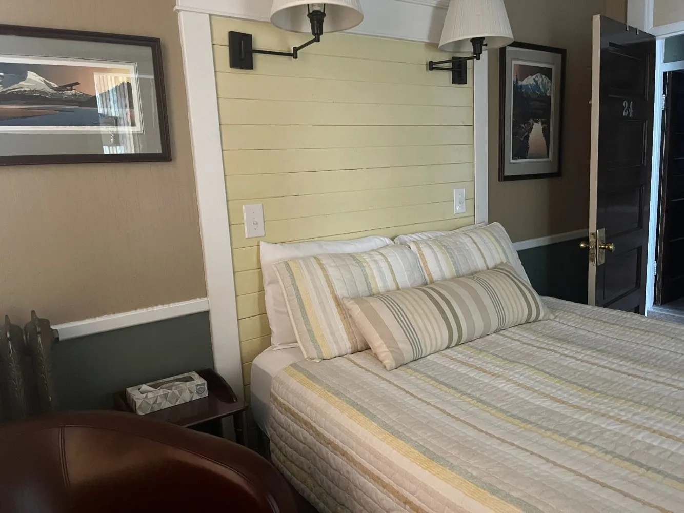 A deluxe queen room with a pale wood-panelled headboard wall, reading lamps and framed prints