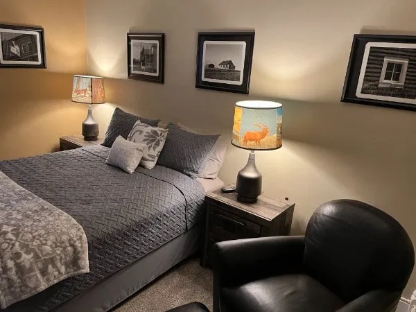 One bedroom of the three-bedroom unit, with a grey quilt, a leather armchair and black-and-white prairie photographs